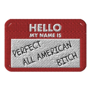 May include: A red embroidered name tag with the text "HELLO MY NAME IS" at the top. Below, a white rectangle features the words "PERFECT ALL AMERICAN BITCH" in black, angled text.