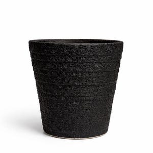 May include: A black textured ceramic planter with a wide opening and a slightly tapered shape. The planter has a rough, layered surface and a light-colored base. This decorative pot is suitable for indoor or outdoor use.