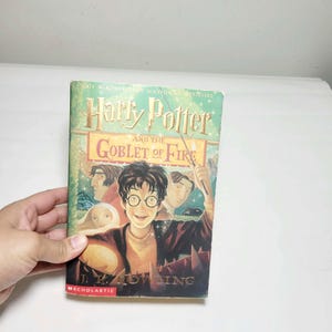 May include: A hardcover book titled Harry Potter and the Goblet of Fire by J.K. Rowling. The green cover features an illustration of a young person with glasses holding a wand, surrounded by other characters, with the Scholastic logo at the bottom.
