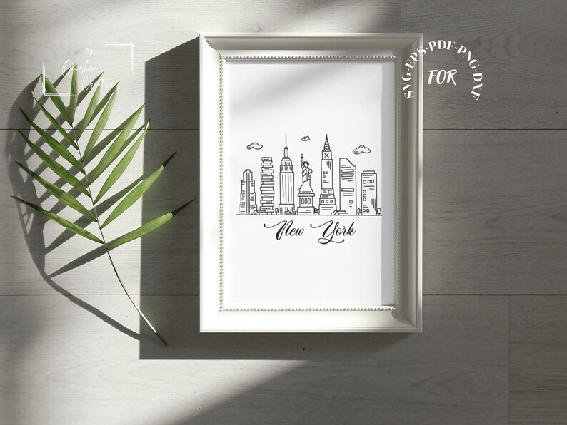 May include: A white framed print with a black and white line drawing of the New York City skyline, including the Statue of Liberty and the Empire State Building. The text "New York" is written in cursive below the skyline.