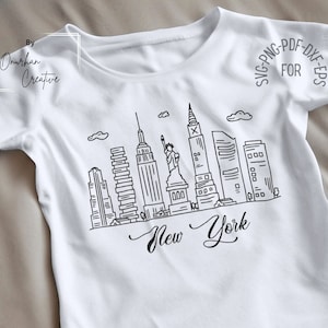 May include: A white t-shirt with a black line drawing of the New York City skyline, including the Statue of Liberty and skyscrapers. The text "New York" is written below the skyline.