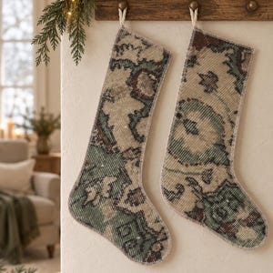 Op de afbeelding: Twee kerstsokken gemaakt van geweven stof in vintage-stijl met een ingewikkeld, vervaagd bloemen- en geometrisch patroon in gedempte tinten saliegroen, beige en donkerbruin, afgewerkt met een eenvoudige lichtgekleurde gestikte rand.