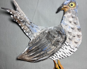 May include: A hand-painted, stylized bird sculpture with a gray, blue, and white color scheme. The bird has a yellow eye, a black beak, and orange feet. The artwork is set against a gray background.