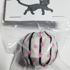 May include: A white and black striped cat toy with pink paw prints. The toy is packaged in a clear plastic bag with a white label that says "Crooked Tail Cat Toys" and a black silhouette of a cat.