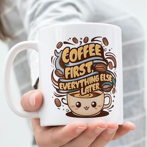 May include: White ceramic mug with a cartoon illustration of a coffee cup with a smiling face. The text on the mug reads "Coffee First Everything Else Later".
