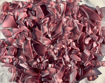 May include: A large pile of small, iridescent purple glass shards. The glass is smooth and polished, with a variety of shapes and sizes.