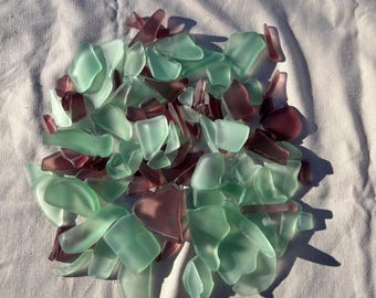 May include: A collection of sea glass in shades of green and purple. The glass pieces are smooth and have been tumbled by the ocean.