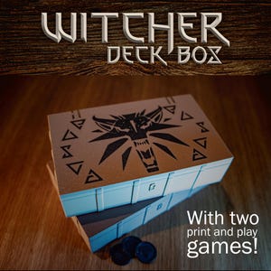 Könnte beinhalten: Gestapelte Kartenbox mit dem Text "Witcher Deck Box" oben. Die Box ist beige mit einem schwarzen Wolfskopf-Design und geometrischen Formen. Der Text "With two print and play games!" befindet sich unten.