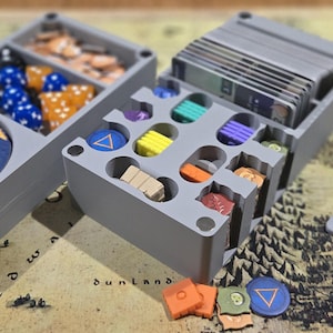 May include: Gray plastic game organizer with compartments for dice, tokens, and cards. Includes a blue disc with a heart design, various colored game pieces, and a card with the word "DESCENT" in blue.
