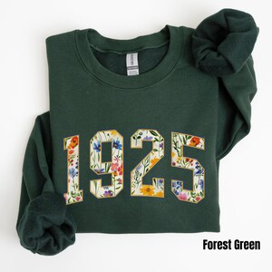 May include: Forest green sweatshirt with a floral print design of the year 1925.
