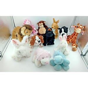 May include: A selection of soft toy animals, including a lion, monkey, kangaroo, dog, giraffe, and bunny. The toys are in various colours, such as brown, pink, white, and black. The toys are made of soft materials.