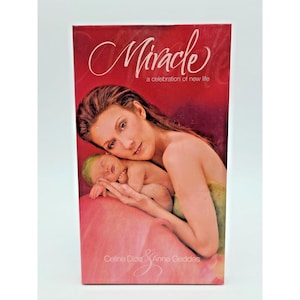 May include: A red book cover with the title "Miracle" in cursive script. The cover features a woman holding a baby, with the text "a celebration of new life" below the title. The names "Celine Dion" and "Anne Geddes" are also visible.