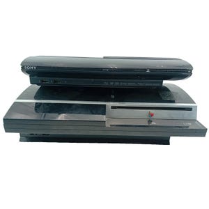 May include: Two black Sony PlayStation 3 consoles stacked on top of each other. The top console is a slim model, while the bottom console is a larger, older model. The consoles are on a white background.