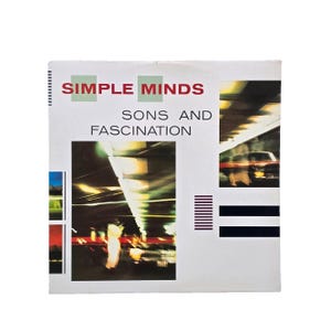 Peut inclure: Pochette d'album vintage pour "Sons and Fascination" de Simple Minds. Le nom du groupe est en rouge au-dessus du titre de l'album. La conception comprend une photo d'une route avec des lumières floues et une voiture.