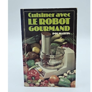 May include: A vintage cookbook titled "Cuisiner avec LE ROBOT GOURMAND" featuring a food processor. The cover has a black background with green and yellow text. The image includes various vegetables and fruits, suggesting recipes.