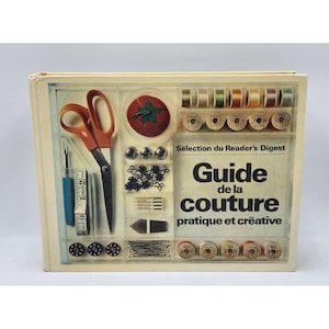 May include: A vintage sewing guide titled "Guide de la couture pratique et créative" with sewing tools on display. The cover shows orange scissors, spools of thread, buttons, and a tomato pin cushion. A measuring tape and other sewing notions are also visible.