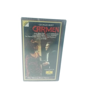 Pode incluir: Uma fita VHS selada da ópera "Carmen" de Georges Bizet, com Agnes Baltsa, José Carreras e Leona Mitchell. A capa mostra duas figuras com roupas de época, com o título em letras vermelhas. The Metropolitan Opera.