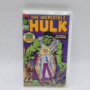 May include: A vintage VHS tape with the comic book cover of "The Incredible Hulk." The cover art features a large green Hulk figure, a smaller figure of Doctor Banner, and the text "Origin of the Hulk!" in a comic book style.