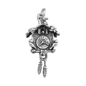 May include: A silver-toned charm in the shape of a cuckoo clock. The clock features a detailed face, birds, and decorative elements. The charm has a loop at the top for attachment and dangling weights at the bottom. A miniature representation of a classic timepiece.