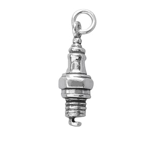 May include: A silver spark plug charm with a loop for attaching to a chain or bracelet. The charm has detailed ridges and a curved end, ideal for jewellery making or as a unique pendant.