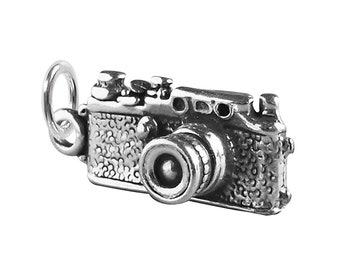 May include: A silver charm in the shape of a vintage camera. The camera has a textured surface and a detailed lens.