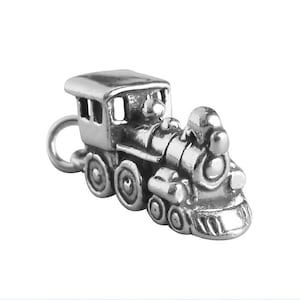 May include: A silver-colored charm in the shape of a classic steam train. The detailed miniature train features a rounded front, a smokestack, and multiple wheels. The charm has a loop for attaching to a bracelet or necklace.