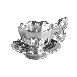 Könnte beinhalten: Ein kleines, silberfarbenes Tee-Set. Die Tasse hat einen gewellten Rand und einen dekorativen Henkel. Die Untertasse hat ebenfalls einen gewellten Rand. Das Set besteht aus glänzendem, reflektierendem Metall.