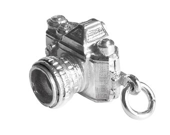 May include: Silver charm in the shape of a vintage camera. The camera has a lens, a viewfinder, and a strap. The charm is detailed and realistic.