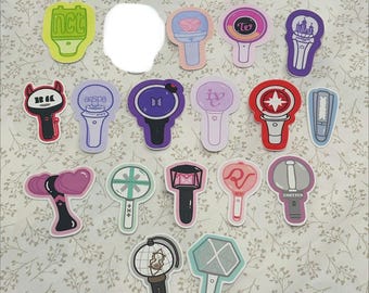 May include: A selection of stickers showcasing diverse designs, including light sticks with logos and text. The stickers are arranged on a floral patterned background. The stickers are in various colours, including pink, purple, and green.