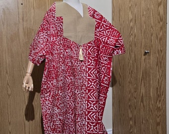 May include: A red and white patterned maxi dress with a tan colored panel at the neckline. The dress has a loose fit and is made of a lightweight fabric.