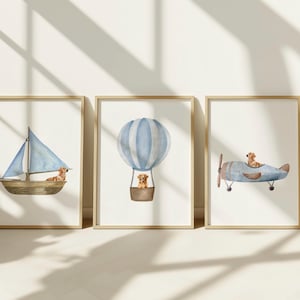May include: Set of three framed watercolor prints featuring a sailboat, hot air balloon, and airplane, each with a golden retriever. The artwork has a soft, pastel color palette with blue and brown tones, perfect for a nursery or children's room.