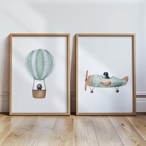 Könnte beinhalten: Zwei gerahmte Kunstdrucke. Einer zeigt einen Aquarell-Heißluftballon in Grüntönen mit einem Hund im Korb. Der andere zeigt einen Hund in einem grünen Vintage-Flugzeug mit braunem Propeller und Flügeln.
