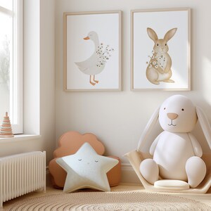 Puede incluir: Dos impresiones enmarcadas en acuarela de un ganso y un conejo con detalles florales cuelgan sobre un juguete de conejo blanco de peluche en una cesta tejida. Una almohada en forma de estrella y una almohada en forma de nube est&aacute;n sobre una alfombra.
