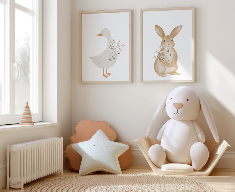 Puede incluir: Dos impresiones enmarcadas en acuarela de un ganso y un conejo con detalles florales cuelgan sobre un juguete de conejo blanco de peluche en una cesta tejida. Una almohada en forma de estrella y una almohada en forma de nube est&aacute;n sobre una alfombra.
