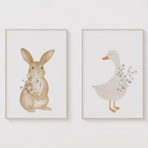 Puede incluir: Dos impresiones art&iacute;sticas enmarcadas con ilustraciones de acuarela de animales. Una muestra un conejo marr&oacute;n sosteniendo flores, y la otra un ganso blanco con pico y patas naranjas, tambi&eacute;n sosteniendo flores. Ambas sobre fondo blanco.