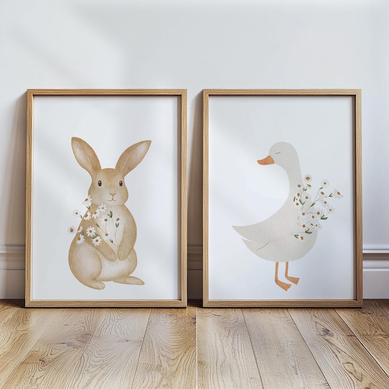 Puede incluir: Dos l&aacute;minas enmarcadas con ilustraciones en acuarela de un conejo y un ganso. El conejo es de color marr&oacute;n claro con un ramo de flores blancas. El ganso es blanco con pico naranja y flores blancas.