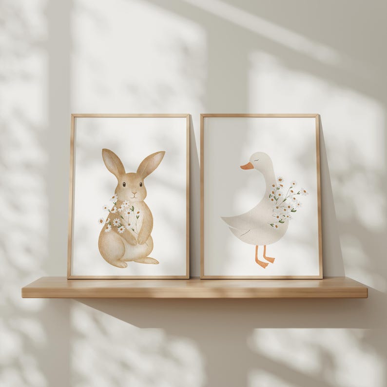 Puede incluir: Dos l&aacute;minas art&iacute;sticas enmarcadas. Una representa un conejo marr&oacute;n claro con flores, la otra un ganso blanco con pico y patas naranjas, tambi&eacute;n con flores. Ambas ilustraciones sobre fondo blanco. Se exhiben en una estanter&iacute;a de madera.