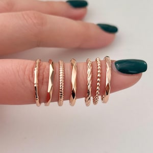 May include: A set of seven gold-toned stacking rings with different textures, including a bamboo design, a diamond pattern, a rope design, and a beaded design.