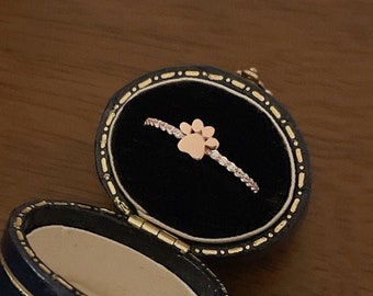 May include: A rose gold ring with a paw print design in a blue ring box.