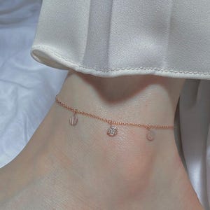 May include: A delicate gold anklet with three charms: a small shell, a round charm with clear stones, and a plain round charm.