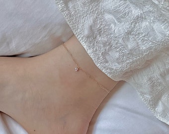 May include: A delicate gold anklet with a small, clear gemstone charm.