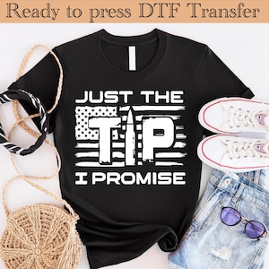 May include: Black t-shirt with a white graphic of an American flag with the words "Just the Tip I Promise" and a bullet in the center.