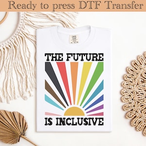 May include: White t-shirt with the text "THE FUTURE IS INCLUSIVE" in black block letters. The design features a colorful sunburst with rainbow-colored rays. The shirt is folded and ready to press.
