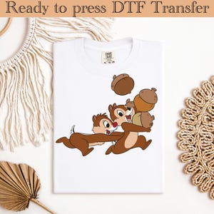May include: White t-shirt featuring a cartoon image of three chipmunks carrying acorns. The chipmunks are brown and white with red noses. The label reads "COMFORT COLORS".