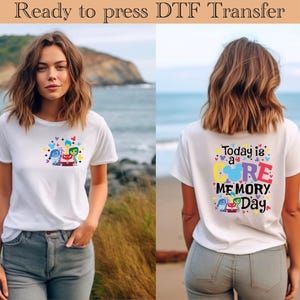 以下が含まれることがあります： インサイド・ヘッドのキャラクターが描かれた白いTシャツ。Tシャツの後ろには「Today is a CORE MEMORY Day」という文字が書かれています。