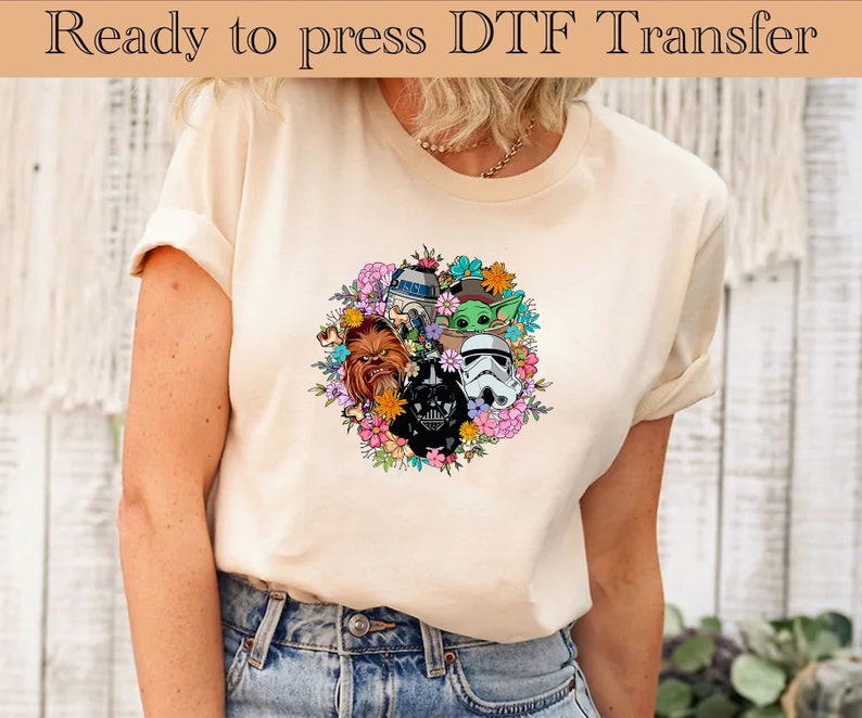 K&ouml;nnte beinhalten: Ein wei&szlig;es T-Shirt mit einem bunten Blumenmuster, das Star Wars-Charaktere zeigt, darunter Darth Vader, Chewbacca, R2-D2 und Baby Yoda.