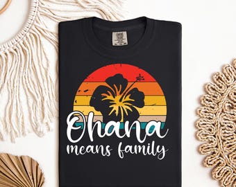 Op de afbeelding: Zwart T-shirt met een vintage-zonnenonderganggrafiek met een gele hibiscusbloem en de tekst "Ohana means family".