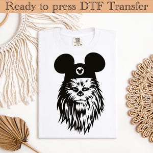 May include: A white t-shirt with a black and white graphic of Chewbacca wearing Mickey Mouse ears and a hat. The graphic includes the text "Ready to press DTF Transfer".