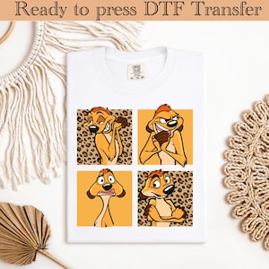 Op de afbeelding: Wit T-shirt met een ontwerp van vier panelen van een cartoon stokstaartje in verschillende poses. Het stokstaartje is oranje en bruin, met een luipaardprint achtergrond in twee panelen. Het shirt heeft bovenaan de tekst "Ready to press DTF Transfer".