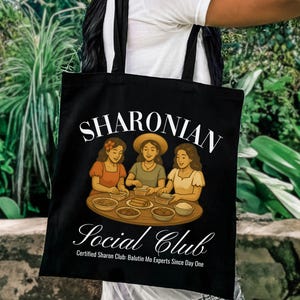 Può includere: Borsa tote nera con la scritta "SHARONIAN Social Club" e un'illustrazione di tre donne. La borsa include anche il testo "Certified Sharon Club: Balutin Mo Experts Since Day One".
